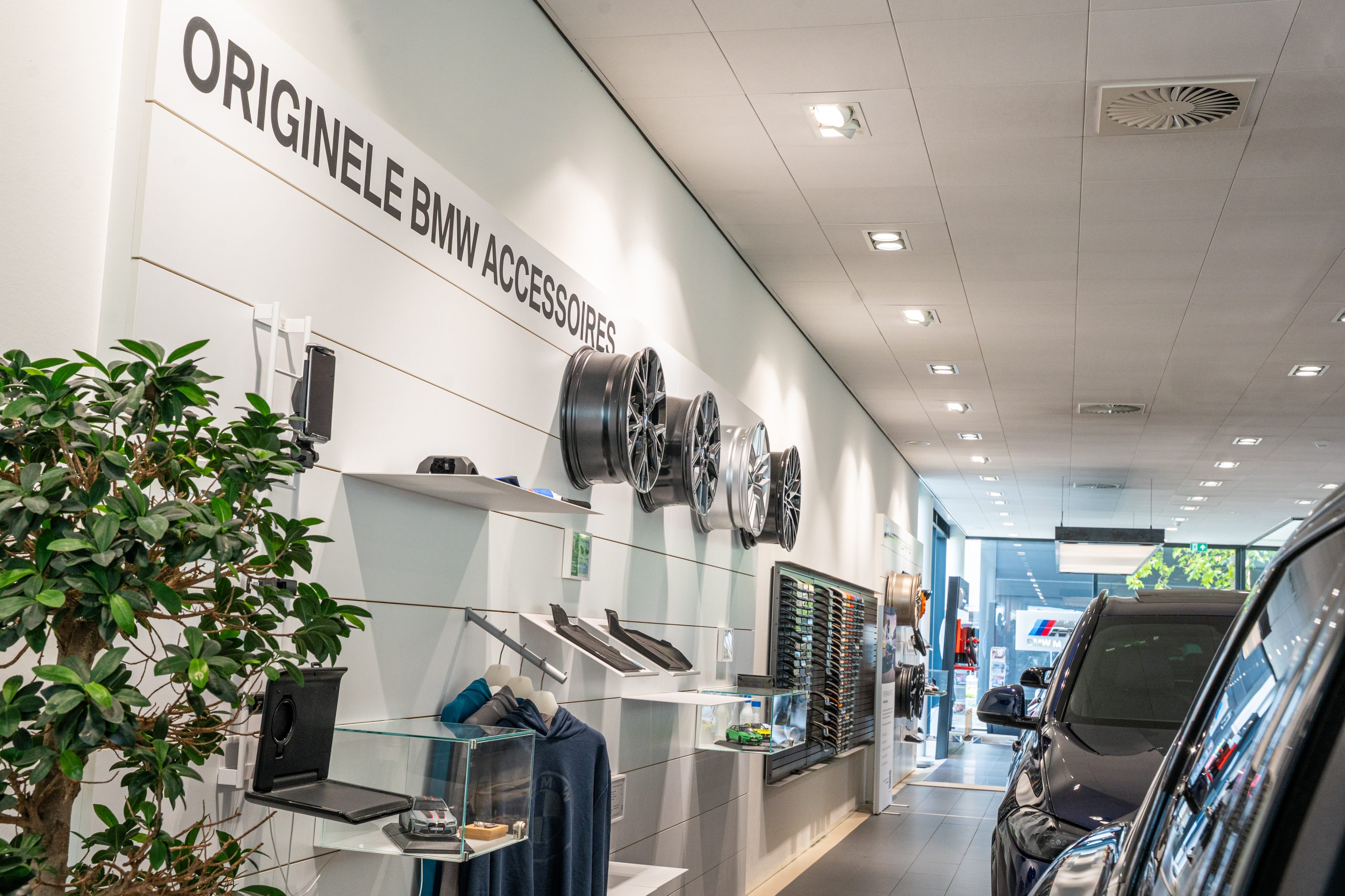De afbeelding toont het interieur van een moderne autodealer of showroom met een wand voor originele BMW-accessoires.
