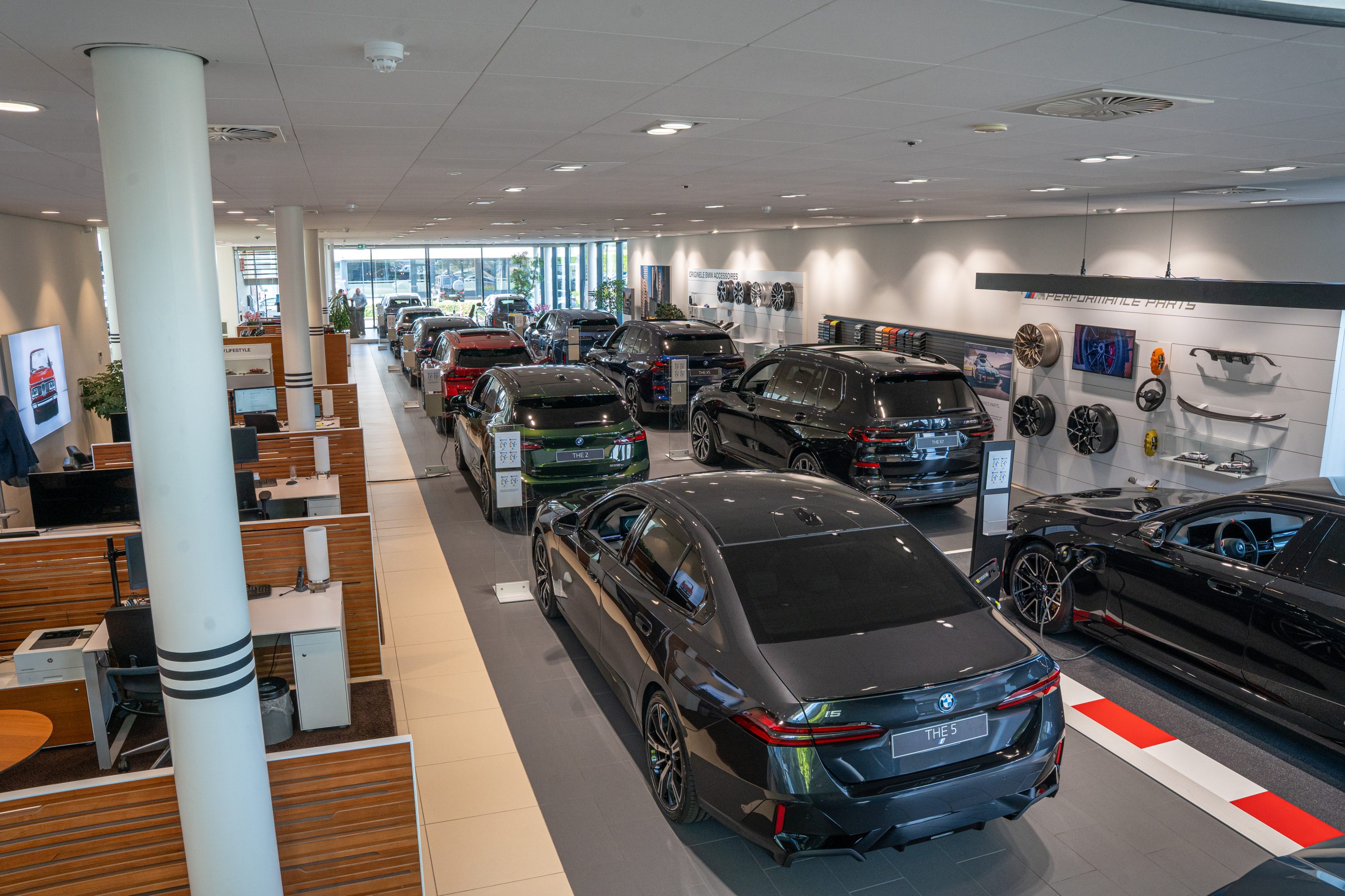 Deze afbeelding toont een moderne BMW-showroom met verschillende nieuwe modellen opgesteld in een rij en diverse auto-onderdelen aan de wand.